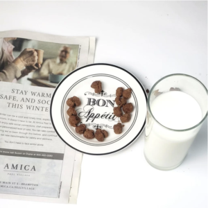 A glass of milk next to a plate of Chin Chin. There is a newspaper in the background.